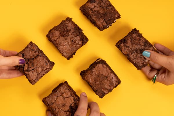 várias mãos pegando brownies num fundo de cor amarela